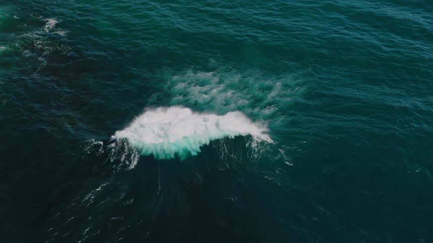 White foam froths and swirls energetically atop the deep bluegreen ocean as a wave rolls through