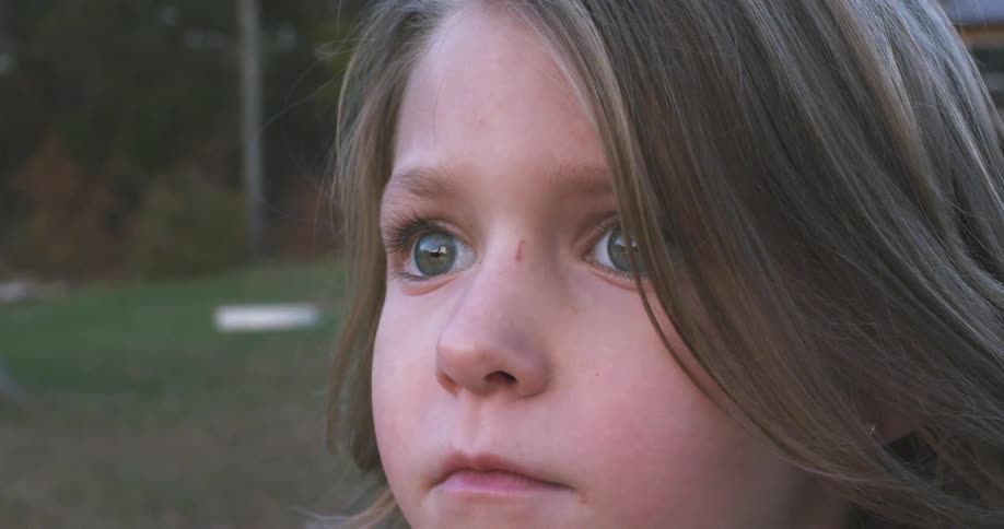 A little girl is standing outside staring intently into the distance