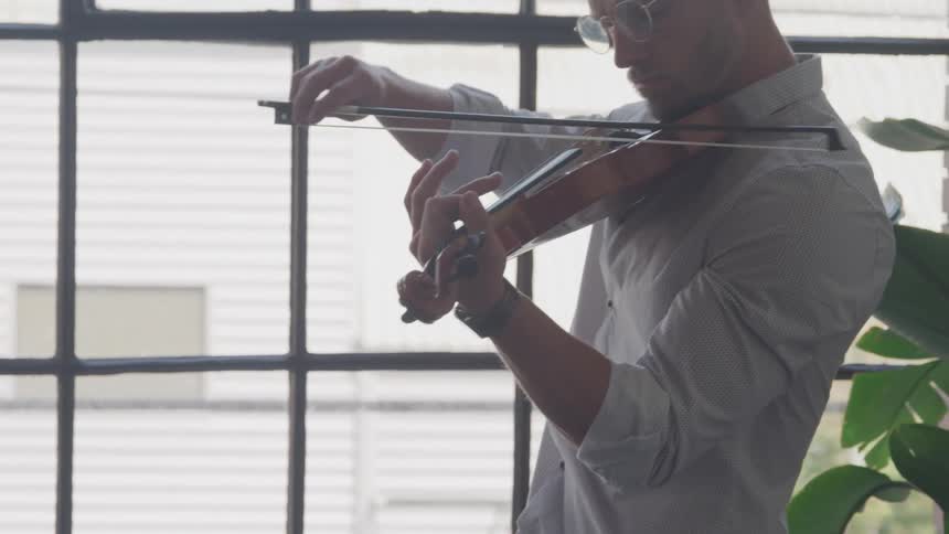 Man playing the violin next to a large window