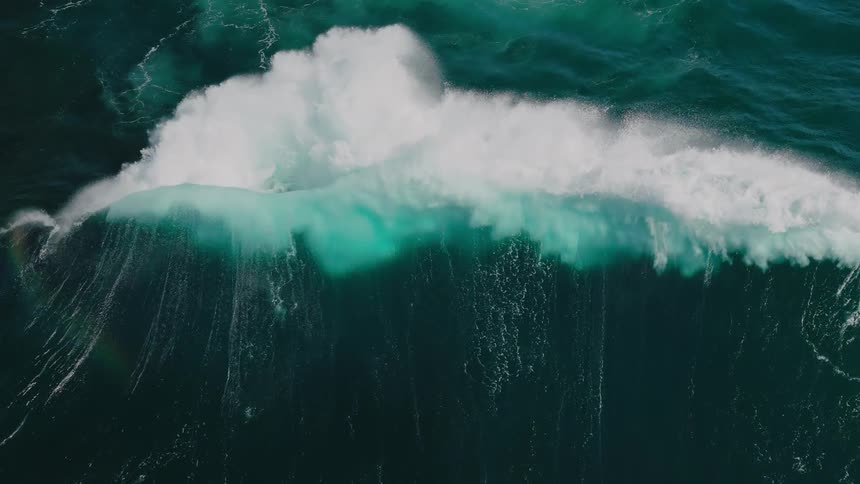 A huge wave crashes in the middle of the ocean creating abundant sea foam