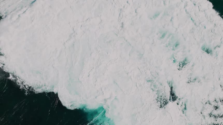 A large wave crashing into the ocean creating a burst of white foam and turquoise water against the dark sea