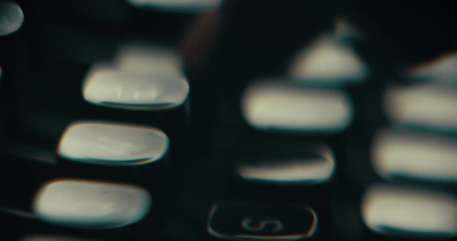 A closeup of fingers pressing typewriter keys in a dimly lit setting