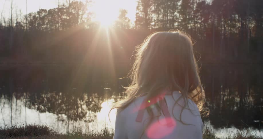 A woman is sitting by the lake watching the sun rise