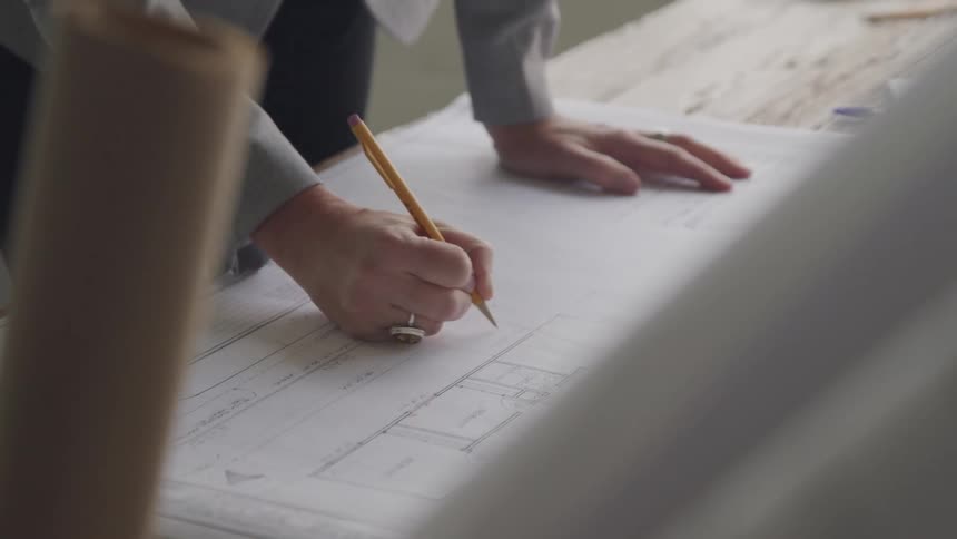 A woman is writing on the blueprints with a pencil