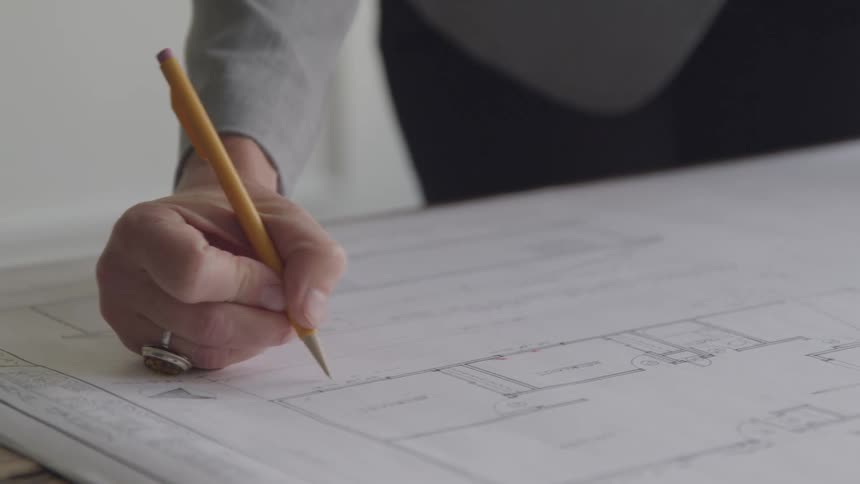 Female architect writing notes with a pencil on a set of blue prints