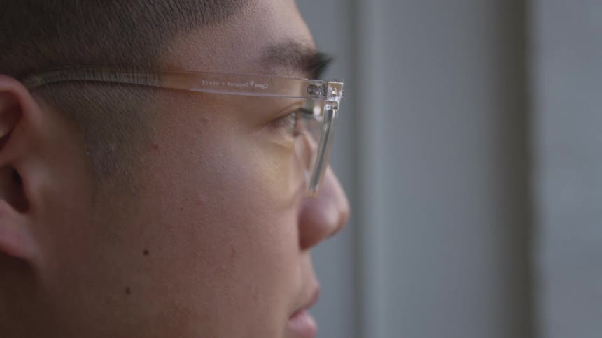 A close up of a young man wearing translucent plastic glasses and looking away