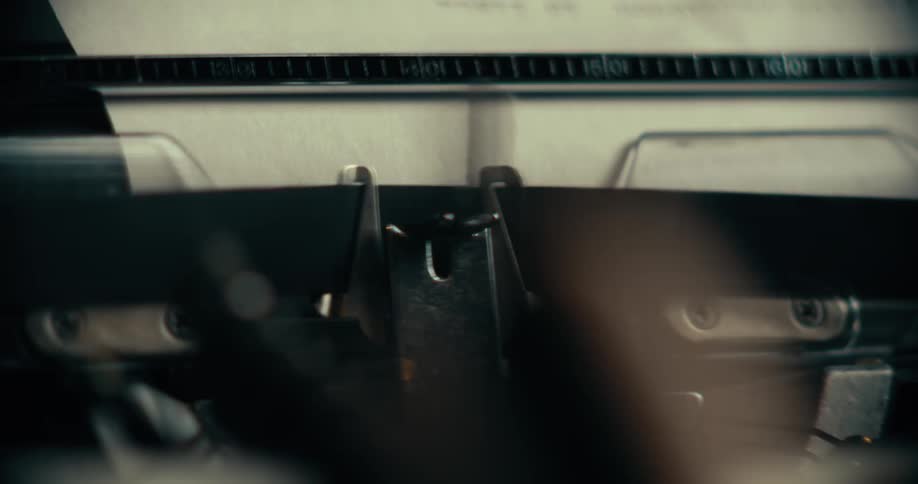 A closeup of typing on a typewriter with fingers blurred in motion and the paper in focus as letters are printed