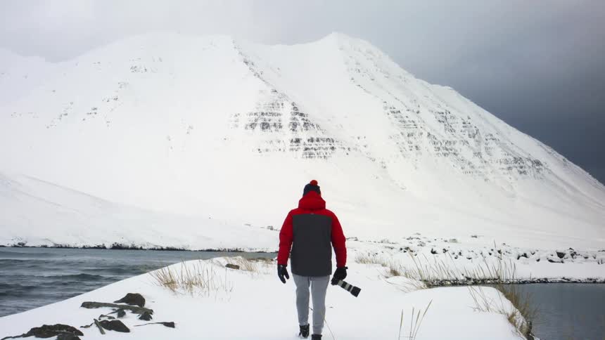A male photographer is walking near snow covered mountains