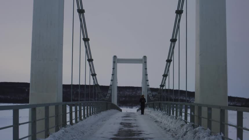 A man is walking on the snow covered bridge