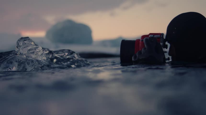 Photographer wearing a wetsuit swimming in the ocean taking a photo of large chunk of ice