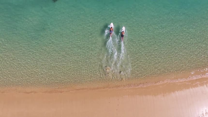 Two men run and jump into the water on their surfboards