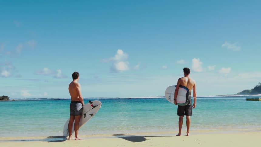 Two surfers holding surfboards standing at the shoreline looking out to the ocean