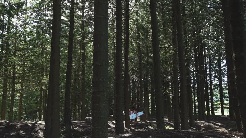 Two men carry their surfboards through the forest