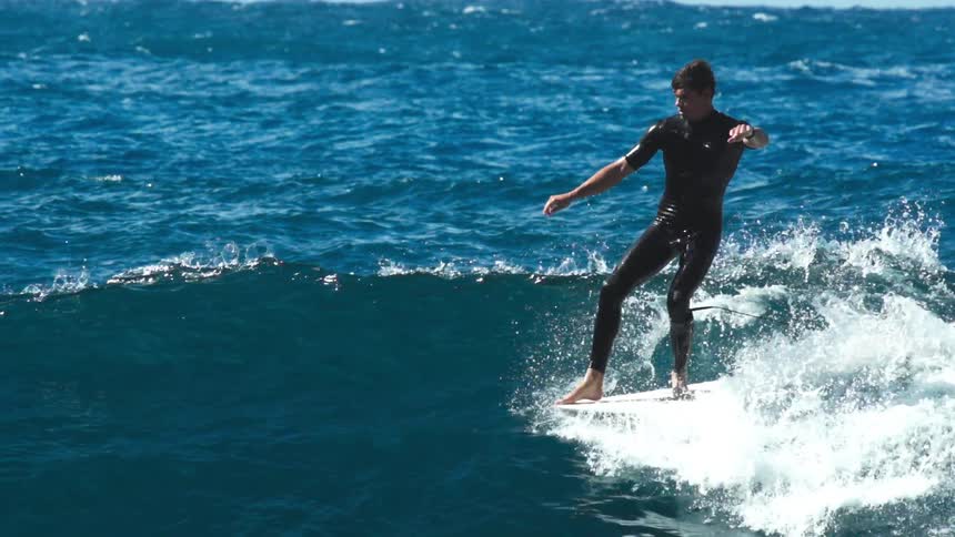 A surfer in a dark wetsuit rides a small wave on a sunny day