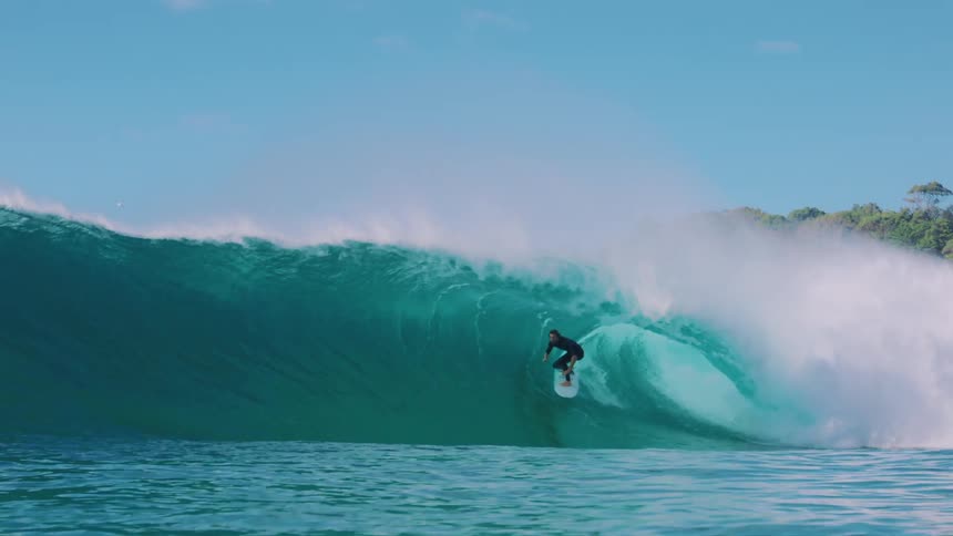 A man is riding a large wave on a sunny day