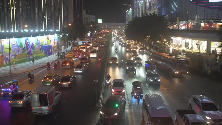 A busy brightly lit city street at night with heavy traffic and numerous vehicles