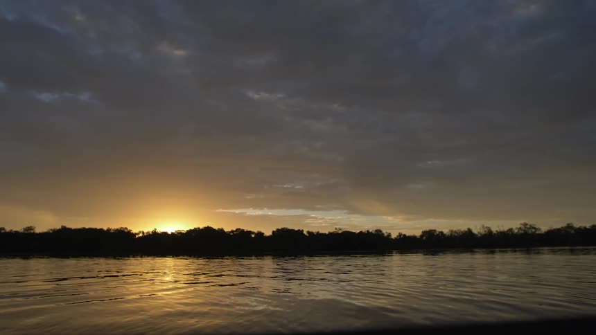 River gently flowing as the sun sets behind the trees in the horizon