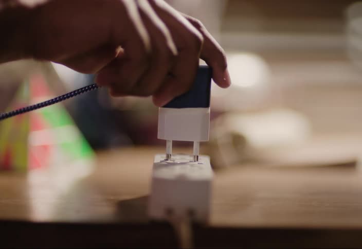 Person plugging in a charging cord into a mounted outlet on a table