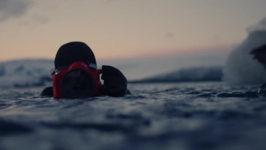 A man is using a large camera to photograph the ice floating in the water