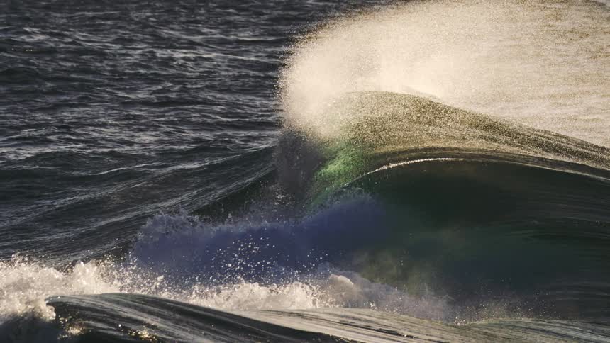 A wave breaking with white foam spraying against the dark textured surface of the ocean