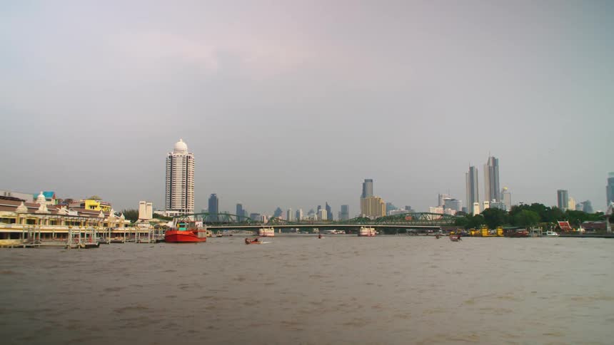 Boats create wakes while moving through the water away from a bridge with the downtown skyline in the background