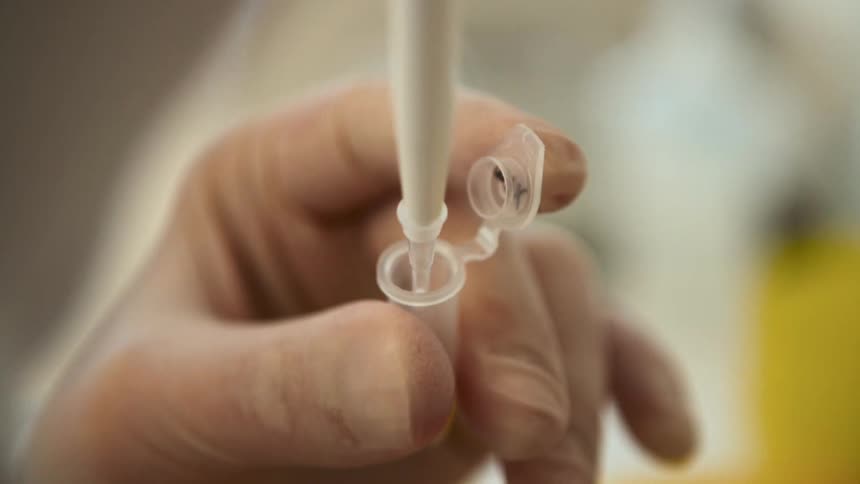 Close up of a persons hand handling a laboratory needle in a small clear vial