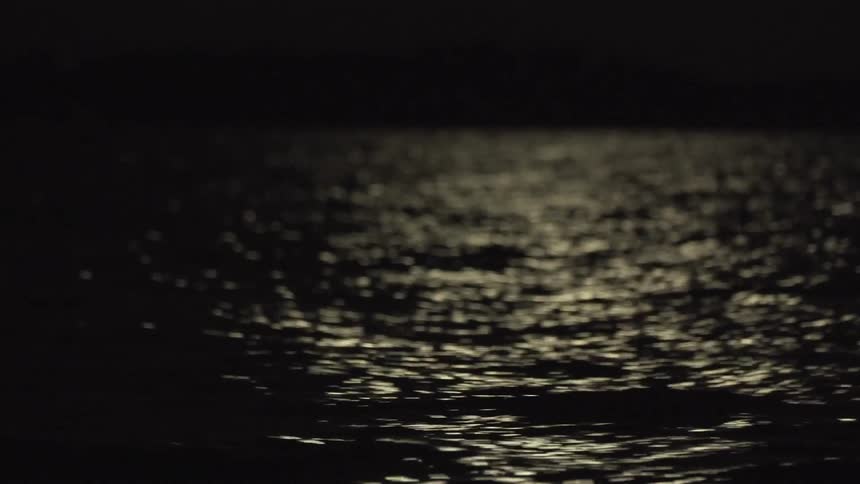 The subtle ripples on a body of water at night reflecting a faint light source and creating a sense of mystery