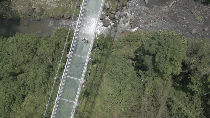 Walking across a glass bottom bridge in the mountains over a river below