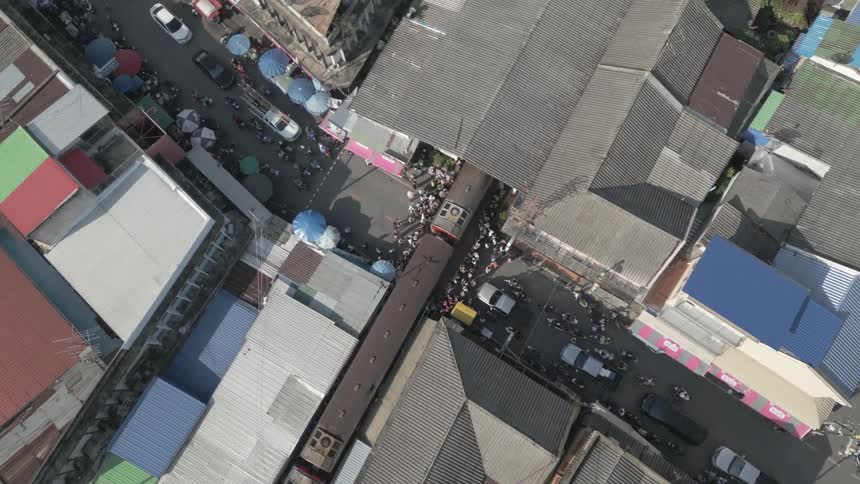 People stand and wait while a slow moving passenger train crosses a residential street and enters a tunnel during the day