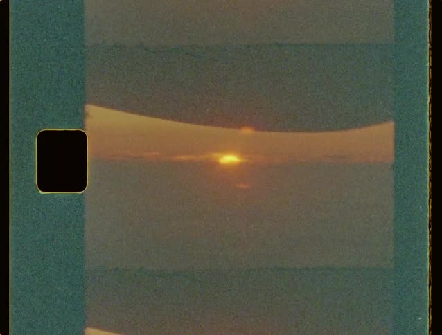 A strip of undeveloped film captures a hazy sunlit horizon line separating a pale sky from a muted landscape