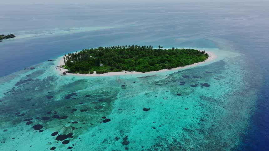 An aerial view of a small lush green island surrounded by crystal clear turquoise waters