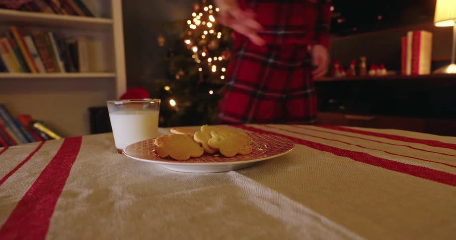 Child in plaid pajamas setting out milk and cookies for santa on dining table on christmas eve