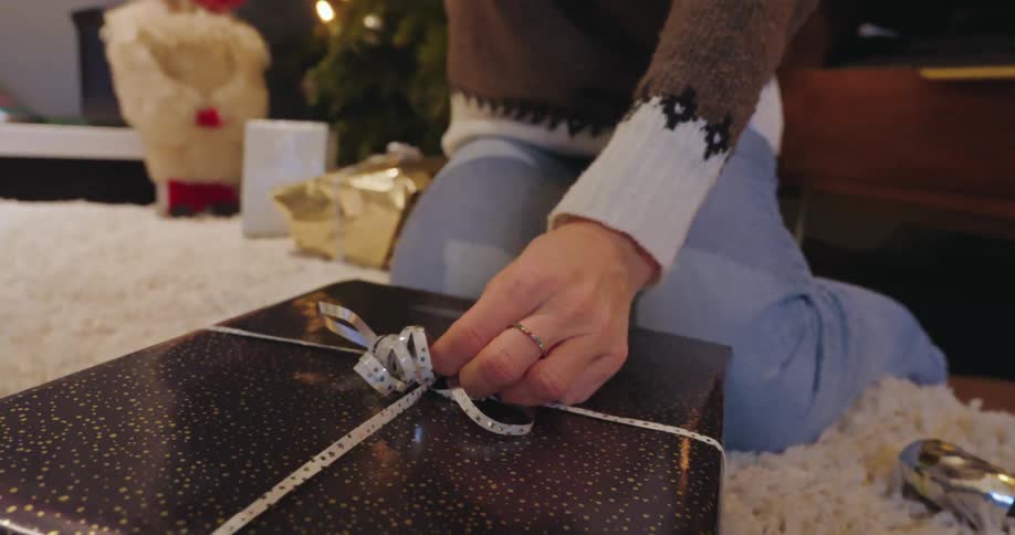 A woman is tying a bow on a christmas present