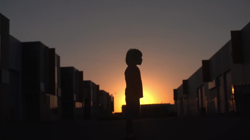 Child standing in the middle of the street at sunset