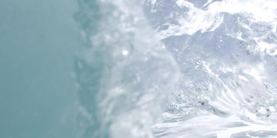 A breaking ocean wave with the clear blue sky above and a glimpse of the shoreline with houses and trees in the background