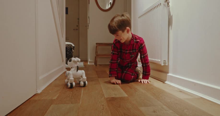 Young boy in red plaid pajamas playing with robotic dog in the hallway
