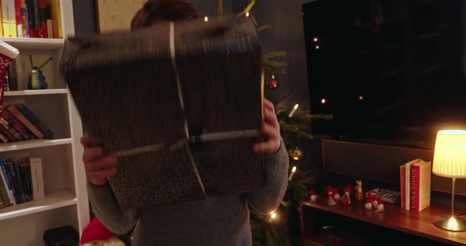 A young boy beams with excitement while holding a wrapped christmas present amidst a festive holiday setting