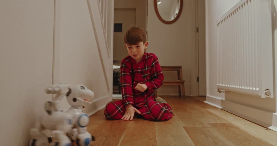 Young boy in plaid pajamas playing with robotic dog in the hallway