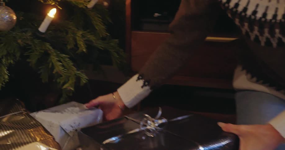 Woman kneeling on the rug places a wrapped present under the christmas tree