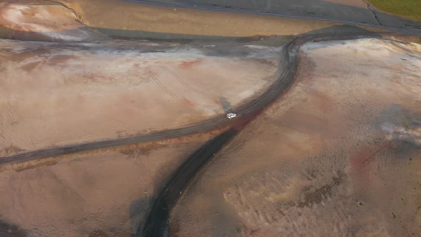 Aerial view of an suv driving on a dirt road through a flooded area near a farmhouse