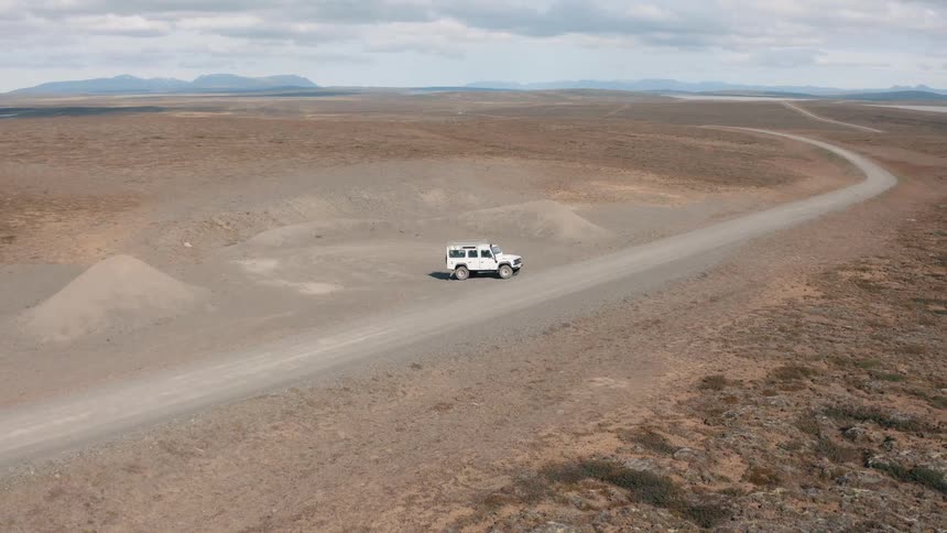 Motor vehicle travels along a rural road passing through arid terrain near the water on a foggy day