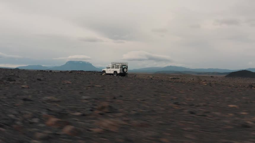 A white truck travels down a dirt road on a dusty plain