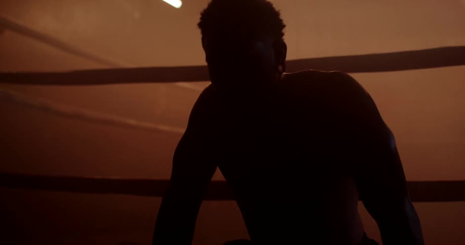 A silhouette of a boxer sits outside the ring surrounded by flashing lights in a dimly lit gym