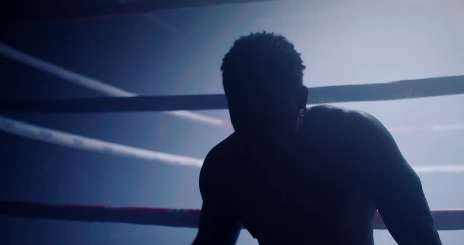 A boxer rests on the boxing ring as lights flash