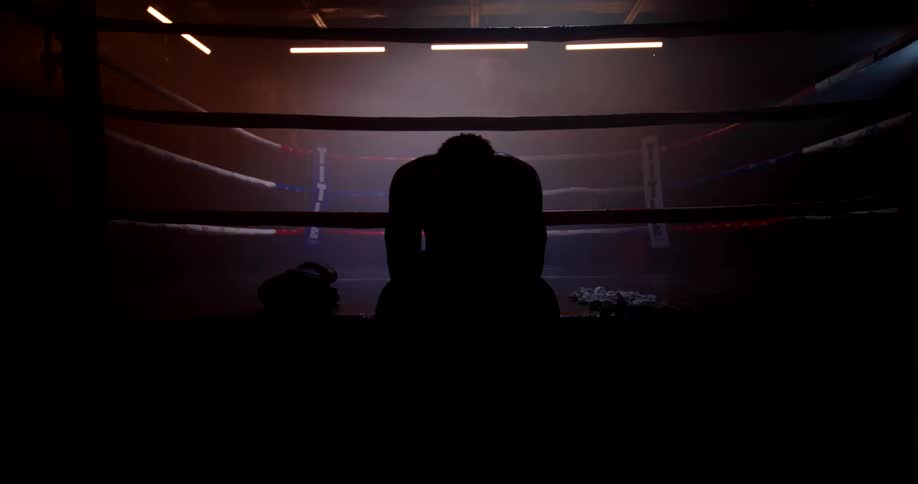 Flashing lights in a gym cast the boxer sitting near the boxing ring into silhouette