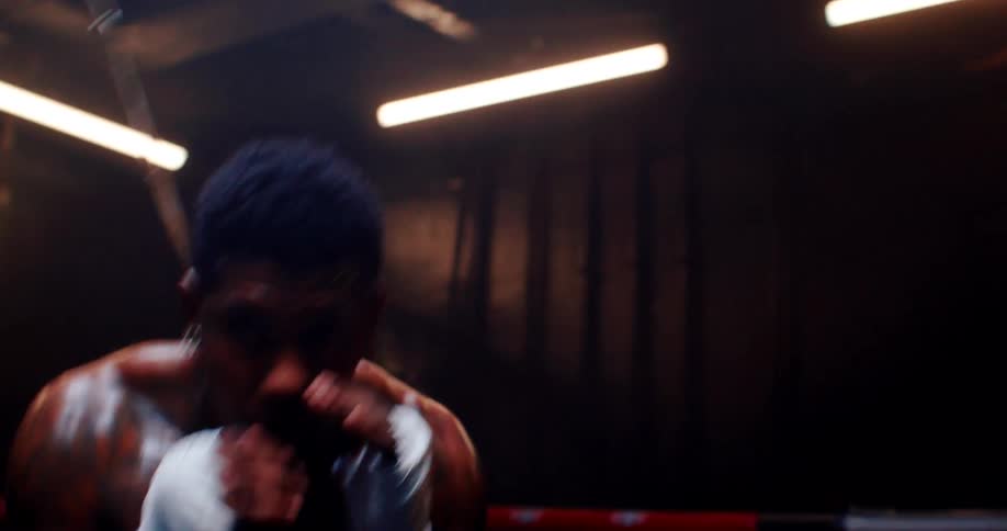A boxer in gloves practices slipping under a taut string in the ring moving left and right to refine evasive techniques