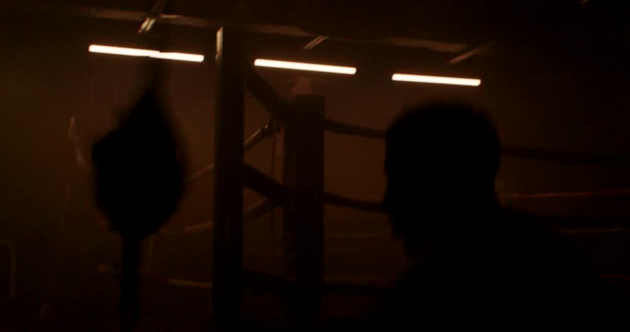 A boxer is punching the bag in the dark gym