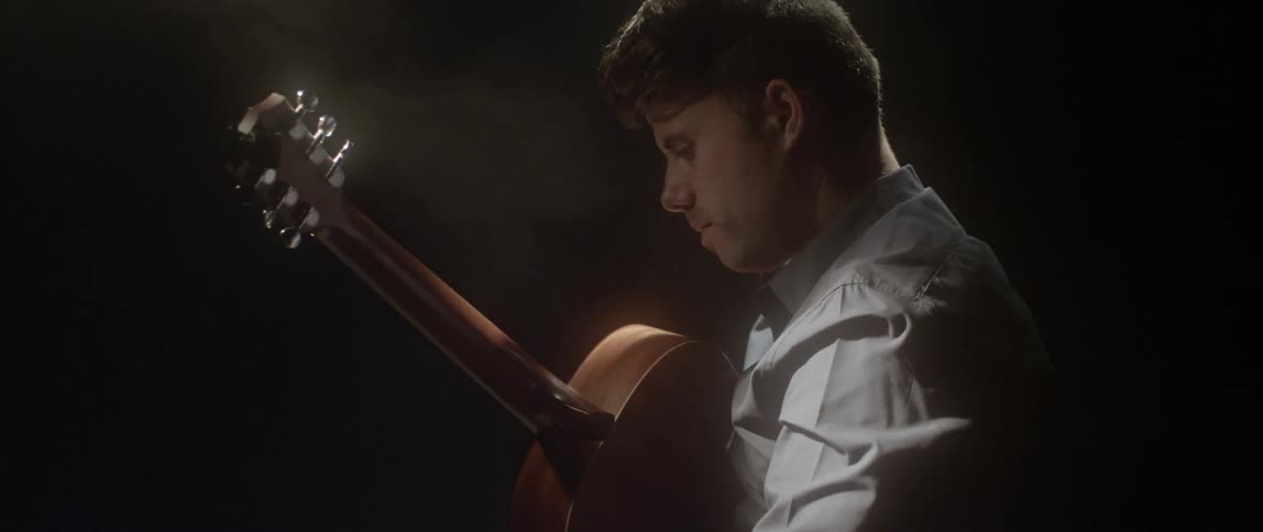 A man is holding a guitar in a dark area