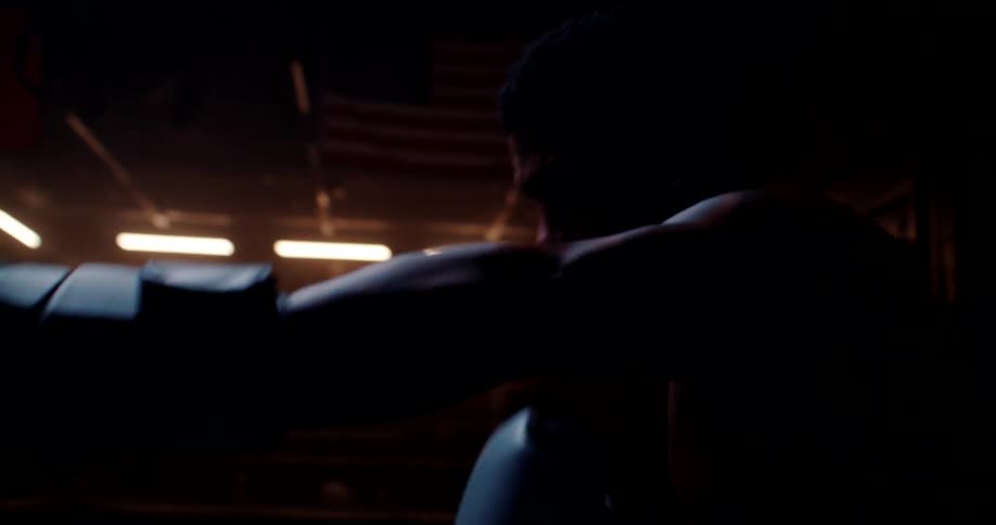A man is boxing by himself in a gym at night time