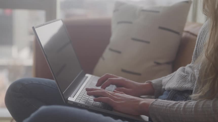 A womans hands typing on a laptop keyboard she is wearing jeans and a light colored top suggesting shes working or browsing from home